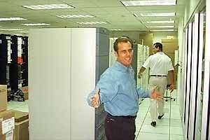 Tim Roberts in a light blue shirt gesturing between equipment cabinets in the data center